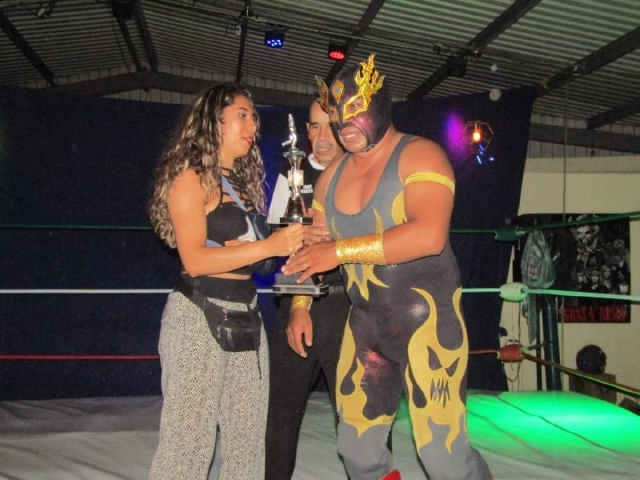 Fuego Dorado recibe de manos de la luchadora Lady Egipcia el trofeo de campeón; el gladiador es uno de los elementos que iniciaron desde hace tres años en esta agrupación.